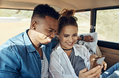 Buy stock photo Shot of a happy young couple using a smartphone on a road trip