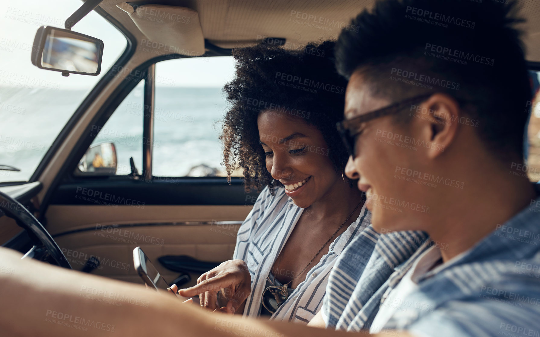 Buy stock photo Shot of a happy young couple using a smartphone on a road trip