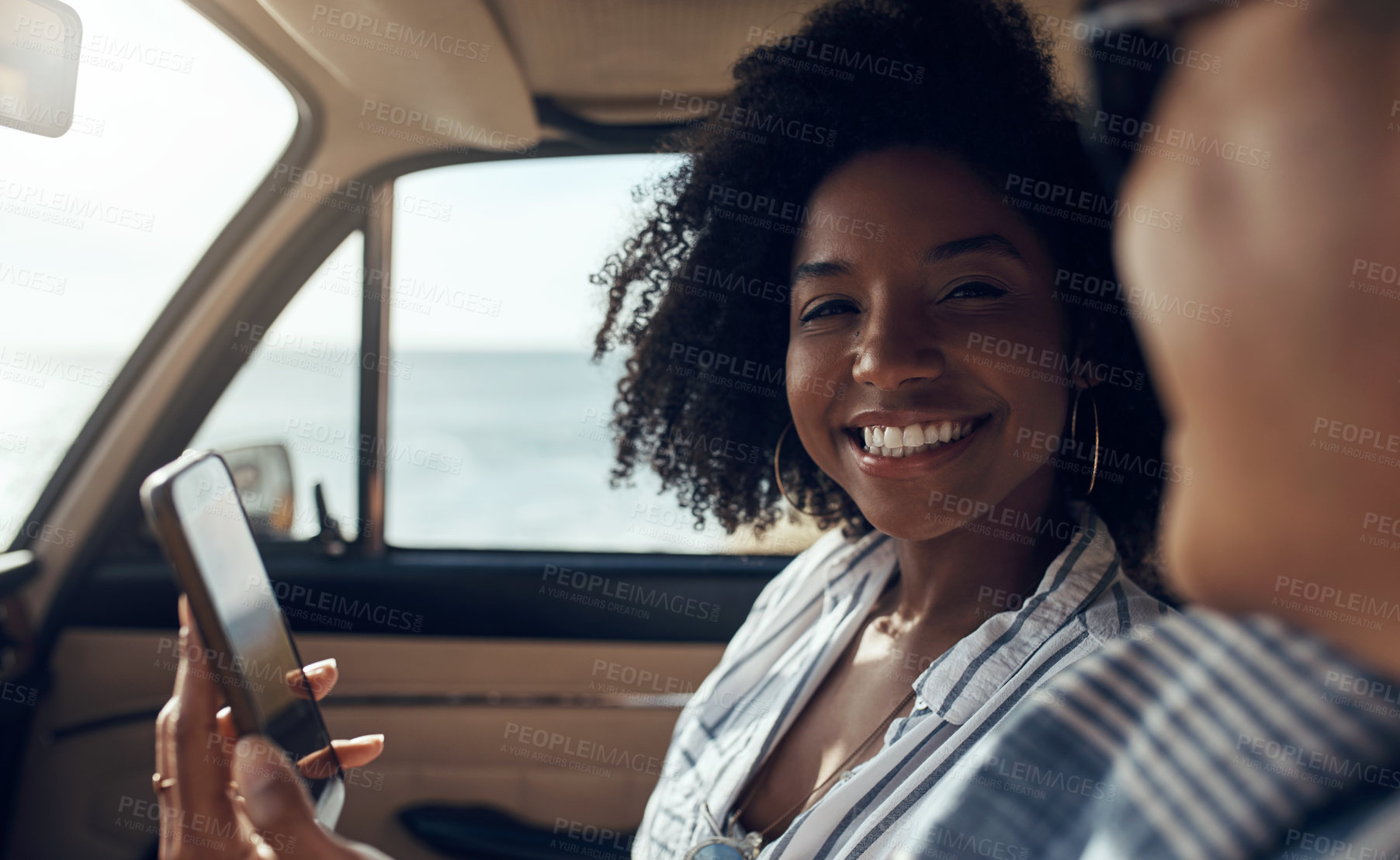 Buy stock photo Shot of a happy young couple using a smartphone on a road trip