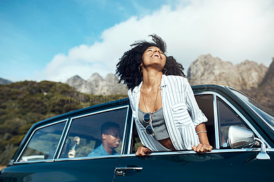 Buy stock photo Shot of a happy young woman leaning out of a car window on a road trip
