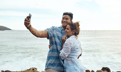 Buy stock photo Shot of a happy young couple taking selfies on a vacation along the coast
