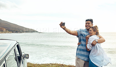 Buy stock photo Shot of a happy young couple taking selfies on a road trip along the coast