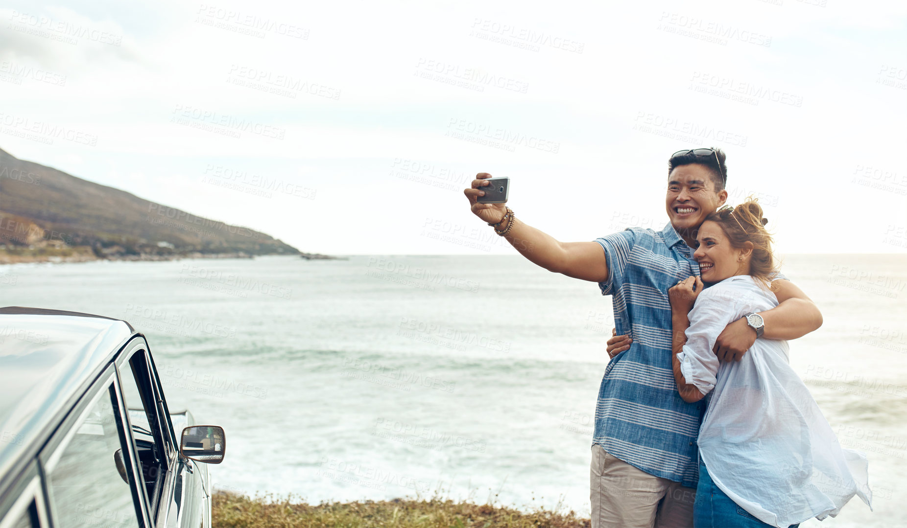 Buy stock photo Shot of a happy young couple taking selfies on a road trip along the coast