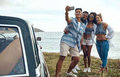 Buy stock photo Shot of a group of happy young friends taking selfies on a road trip along the coast