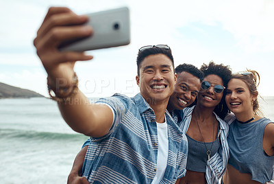 Buy stock photo Shot of a group of happy young friends taking selfies on a vacation along the coast