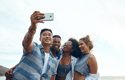 Buy stock photo Shot of a group of happy young friends taking selfies on a vacation along the coast