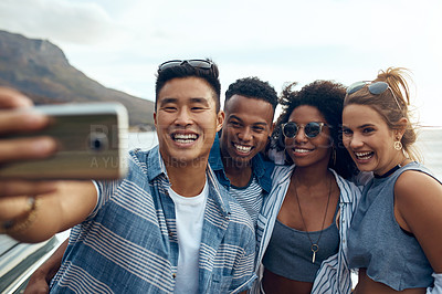 Buy stock photo Shot of a group of happy young friends taking selfies on a vacation along the coast