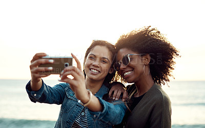 Buy stock photo Shot of two happy young friends taking selfies on a vacation along the coast