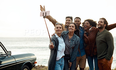 Buy stock photo Shot of a group of happy young friends taking selfies on a road trip along the coast