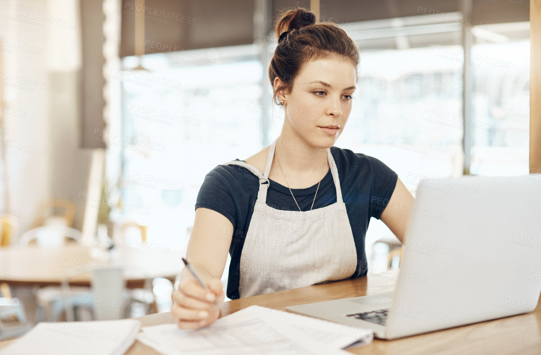 Buy stock photo Shot of a young cafe owner using her laptop and doing paperwork in her shop