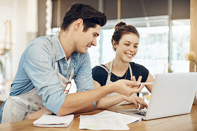 Buy stock photo Shot of two cafe owners having a discussion while using a laptop in their shop