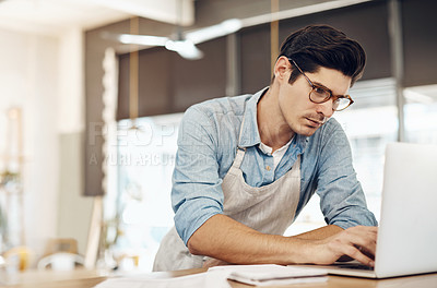 Buy stock photo Shot of a young cafe owner using his laptop and doing paperwork in his shop