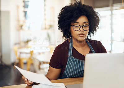Buy stock photo Shot of a young cafe owner using her laptop and doing paperwork in her shop
