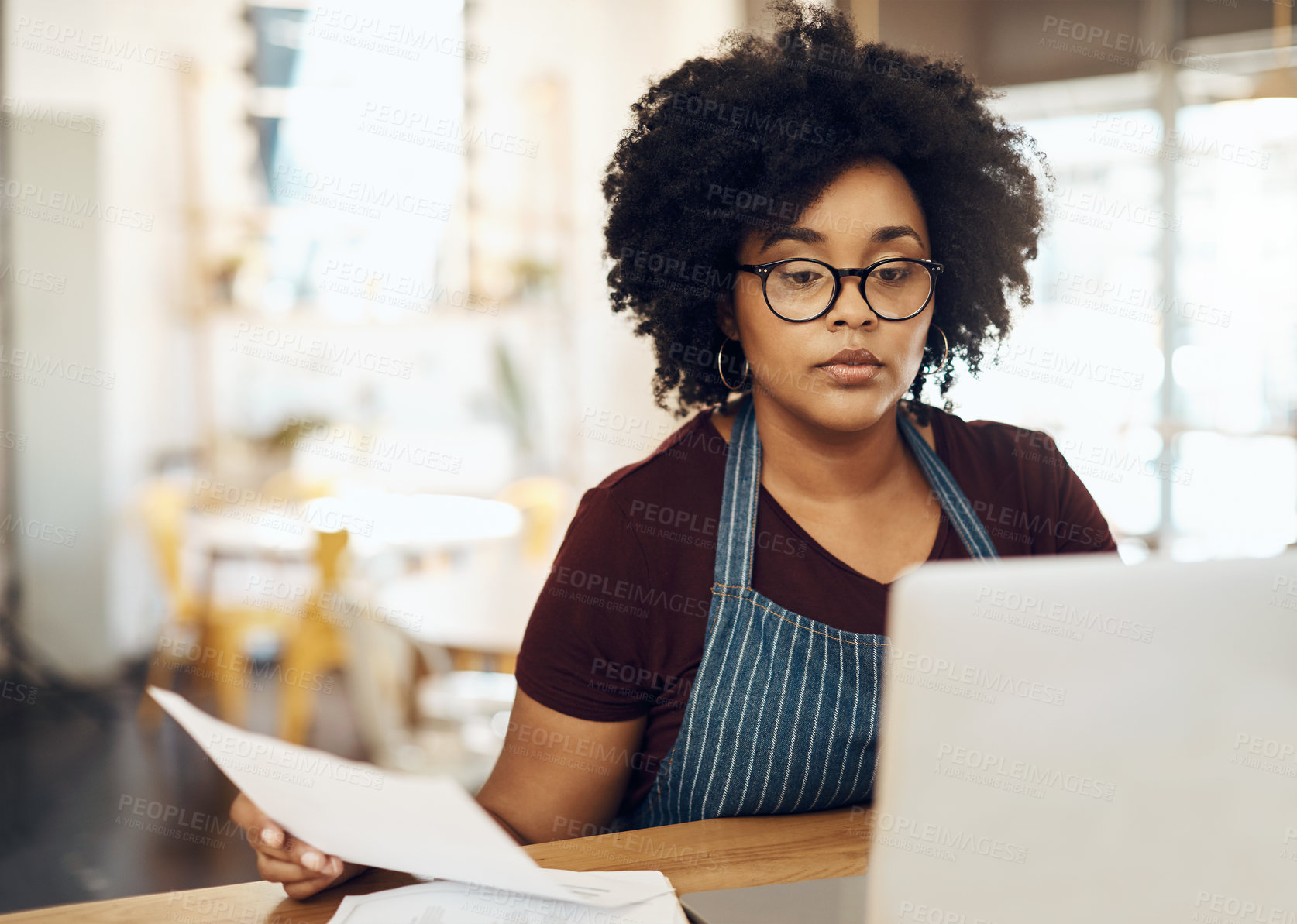 Buy stock photo Shot of a young cafe owner using her laptop and doing paperwork in her shop