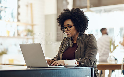 Buy stock photo Cropped shot of a young woman enjoying a cup of coffee while using her laptop in a cafe