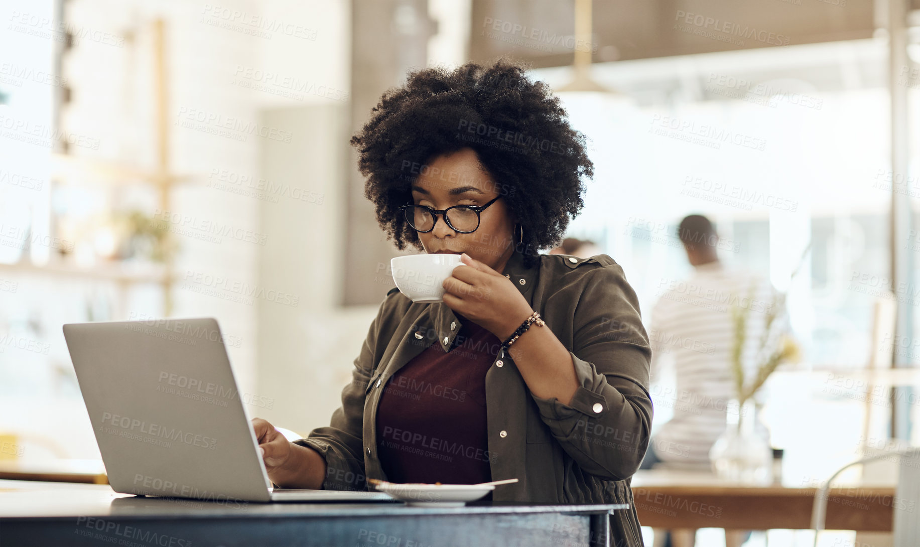 Buy stock photo Cropped shot of a young woman enjoying a cup of coffee while using her laptop in a cafe