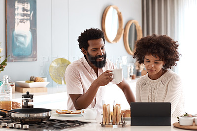 Buy stock photo Shot of a couple looking at something on a digital tablet while having breakfast at home