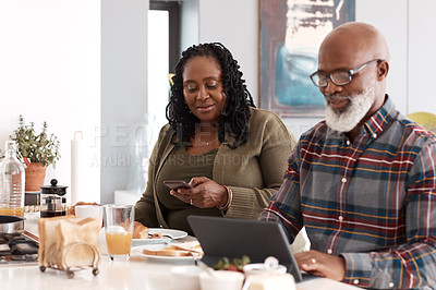 Buy stock photo Shot of a mature couple using their digital devices while having breakfast together at home