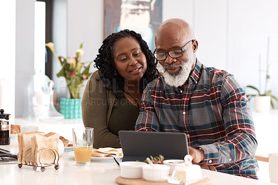 Buy stock photo Shot of a mature couple using a digital tablet while having breakfast together at home