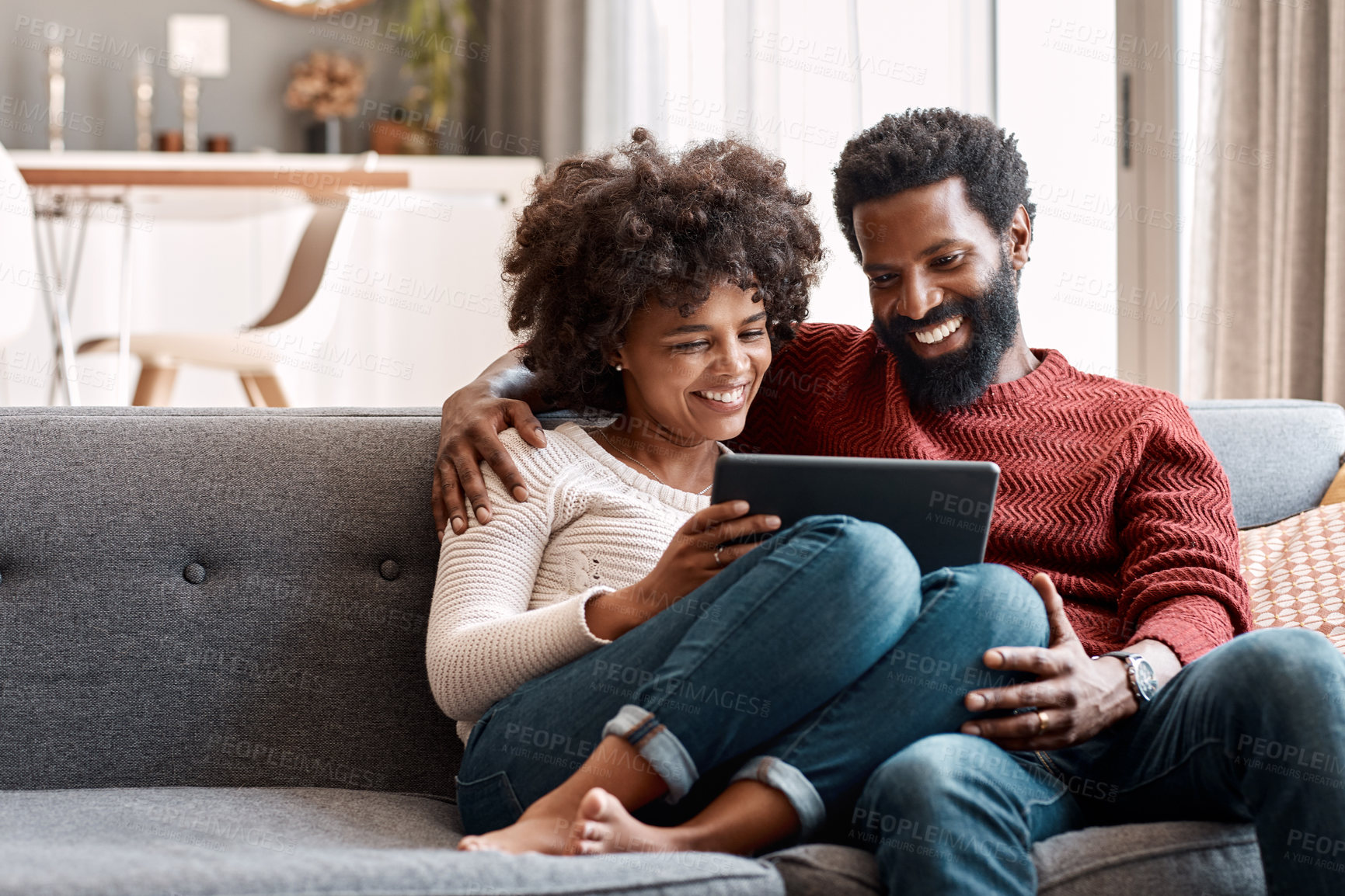 Buy stock photo Shot of an affectionate couple using a digital tablet while relaxing on the sofa at home