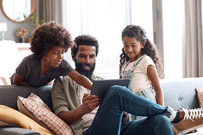 Buy stock photo Shot of two adorable young siblings using a digital tablet while bonding and relaxing with their father at home