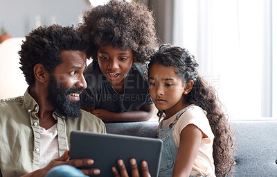 Buy stock photo Shot of two adorable young siblings using a digital tablet while bonding and relaxing with their father at home