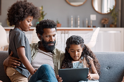 Buy stock photo Shot of two adorable young siblings using a digital tablet while bonding and relaxing with their father at home