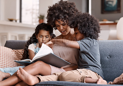 Buy stock photo Shot of a happy young mother reading a book and spending time with her two children at home