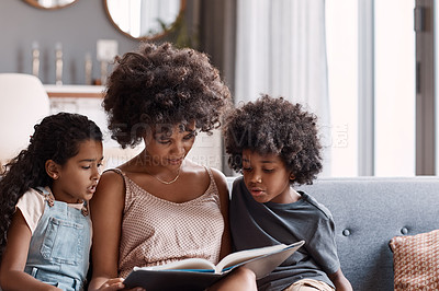 Buy stock photo Shot of a happy young mother reading a book and spending time with her two children at home