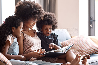 Buy stock photo Shot of a happy young mother reading a book and spending time with her two children at home