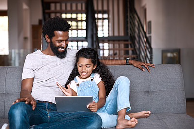 Buy stock photo Shot of an adorable little girl using a digital tablet while bonding and spending time with her father at home