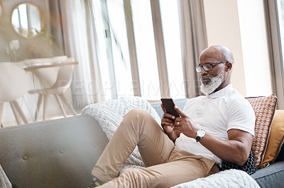 Buy stock photo Shot of a mature man using a cellphone while relaxing on a sofa at home
