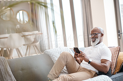 Buy stock photo Shot of a mature man using a cellphone while relaxing on a sofa at home