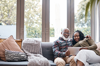 Buy stock photo Shot of a mature couple using a digital tablet while relaxing together on a sofa at home
