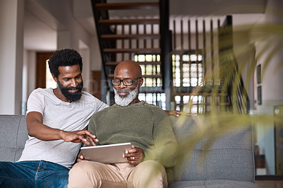 Buy stock photo Shot of a happy senior man using a digital tablet while spending some time with his adult son at home