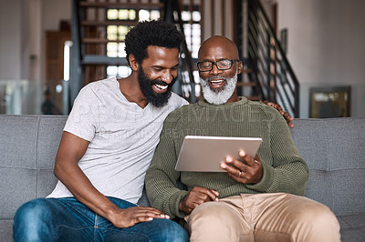 Buy stock photo Shot of a happy senior man using a digital tablet while spending some time with his adult son at home