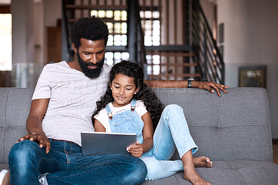 Buy stock photo Shot of an adorable little girl using a digital tablet while bonding and spending time with her father at home