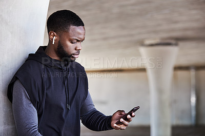 Buy stock photo Cropped shot of a handsome young male athlete checking his phone while working out in the city