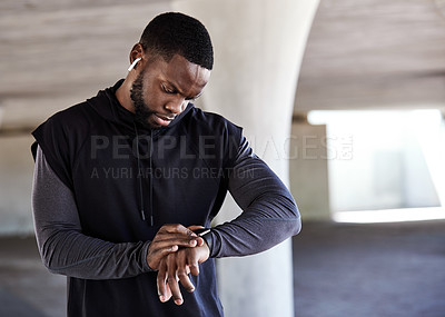 Buy stock photo Cropped shot of a handsome young male athlete checking his watch while working out in the city