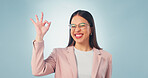Perfect, portrait and happy woman in studio for business success on a blue background. Female person, positive employee or smile with glasses, emoji or OK sign for perfection, accuracy or review