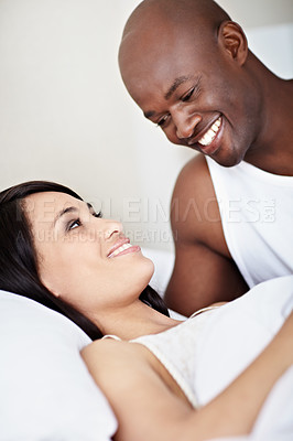 Buy stock photo Shot of a young couple laughing while lying in bed together