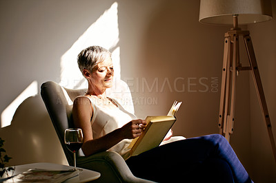 Buy stock photo Shot of a mature woman sitting in a chair reading in the sunlight