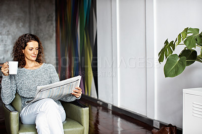 Buy stock photo Shot of a mature woman sitting in her living room drinking a coffee and reading the newspaper