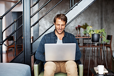 Buy stock photo Shot of a mature man sitting on a chair in his living room using a laptop