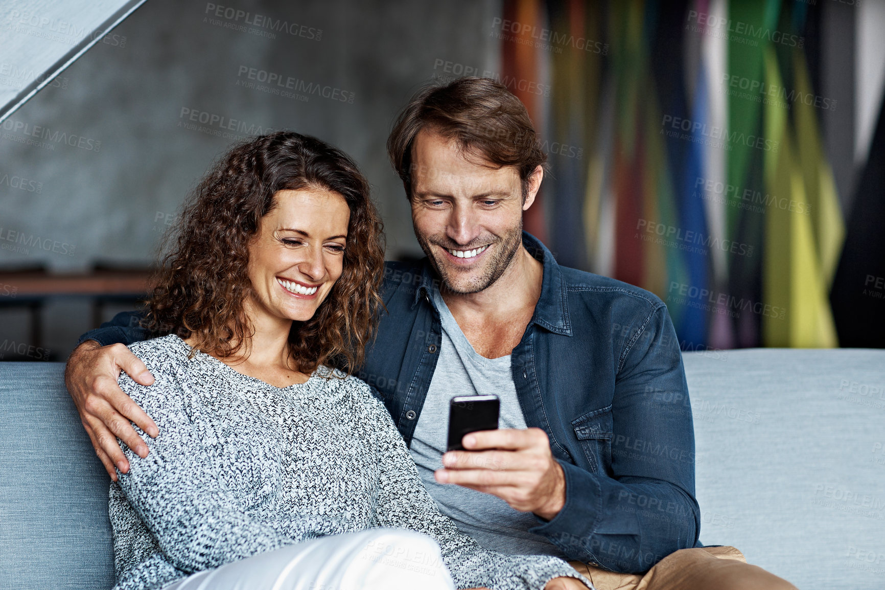 Buy stock photo Shot of a mature couple using a cellphone while sitting on their living room sofa
