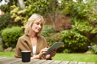 Buy stock photo Shot of a mature woman sitting at a table in her yard using a digital tablet
