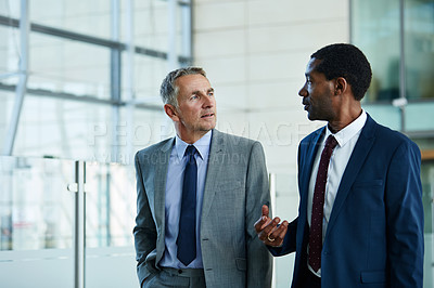 Buy stock photo Shot of two businessmen walking together and talking together in the lobby of an office building