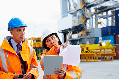 Buy stock photo Shot of two dock workers looking through paperwork while standing in a dockyard