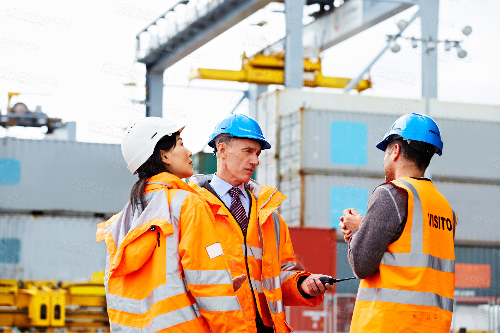 Buy stock photo Shot of three workers talking together while standing on a commercial dock