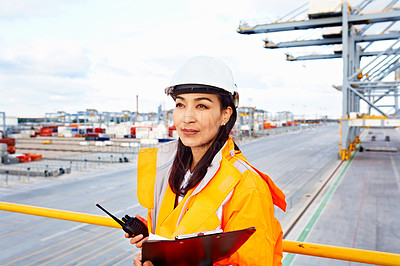 Buy stock photo Shot of a woman in workwear holding a clipboard and walkie talkie while standing on a large commercial dock